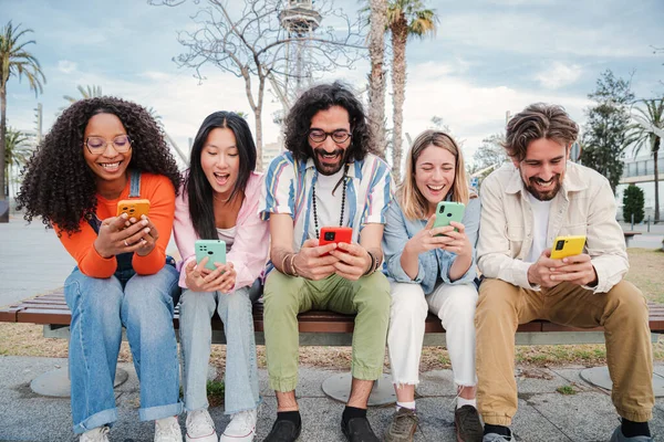 Bir grup en iyi arkadaş cep telefonu uygulamalarını kullanarak bir bankta oturup mesajlarını paylaşarak eğleniyor ve gülümsüyor. Sosyal medyada cep telefonuyla sohbet eden mutlu gençler birlikte eğleniyorlar.
