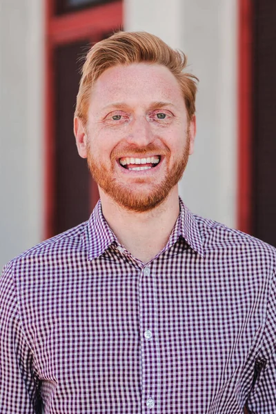 Vertical individual portrait of a formal joyful redhead formal guy standing outdoors smiling and looking at camera. Front view of positive young adult employee man laughing with friendly expression
