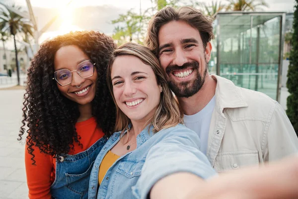 Üç yetişkin arkadaş gülümsüyor selfie çektirip birlikte eğleniyorlar. Arkadaşlıklarını kutlayan bir grup çok ırklı neşeli insan. İki kadın ve olumlu ifadeli bir erkek.