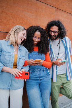 Dikey portre. Arkadaşlarına komik mesajlar yollayan bir kadın cep telefonunu kullanıyor. İnternette akıllı telefonla gezinen gülümseyen arkadaşlar, cep telefonlu gençler.