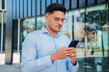 Yeni başlayan yakışıklı bir iş adamı ya da tezgahtarın e-posta göndermek ya da haber okumak için cep telefonunu kullanmasının portresi. Ofis çalışanı internette ciddi bir ifadeyle akıllı telefonuyla geziniyor. Telefonu olan yönetici erkek.