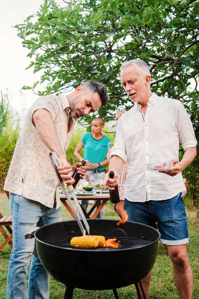 Vertical portrait of a pair of middle aged men cooking meat on a barbeque good party at home backyard. Two mature handsome friends or family grilling on a bbq lunch celebration having fun together