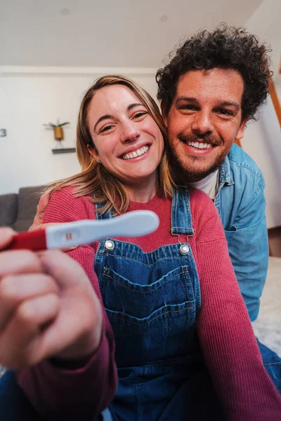 ハッピーな若いカップルの垂直な肖像画は カメラで彼らの肯定的な妊娠検査を示す興奮した笑顔 夫と妻は 彼らが彼らの手に捕食者を抱えている赤ちゃんを期待していることを祝います — ストック写真