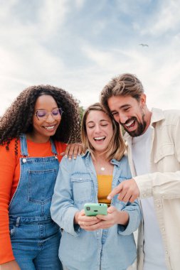 Bir grup arkadaşın, cep telefonuyla eğlenirken, sosyal medyada komik videolar izlerken, oyun oynarken, mesajlar gönderirken dikey portresi. Genç mutlu insanlar bir telefon kullanarak gülümsüyor ve gülüyorlar.