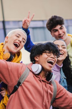Birlikte eğlenen genç bir arkadaş grubunun dikey portresi. Mutlu öğrenciler heyecanlı bir ifadeyle gülümsüyor. Kampüsün dışındaki üniversite kampüsünde gülen çok ırklı arkadaşlar.