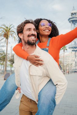 Romantik bir randevuda birlikte eğlenen çiftin dikey portresi. Gülümseyen adam kız arkadaşını sırtında taşıyor, o da işaret ediyor. Mutlu erkek, kız arkadaşını omuzlarında taşıyor. Yüksek