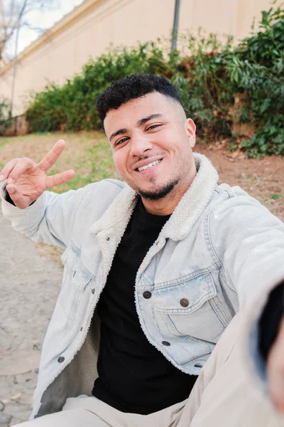 Gülümseyen genç bir Arap 'ın dikey portresi mutlu bir ifadeyle kameraya bakarken selfie çekiyor. Umursamaz adam tatmin edici bir tavırla poz veriyor. Barış işareti yapan gençlerin ön görüntüsü