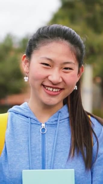一个年轻的中国女学生面带微笑地看着高中的镜头 垂直地把他的个人画像合拢起来 亚洲女孩站在校园里笑着 满面春风地凝视着前方 — 图库视频影像