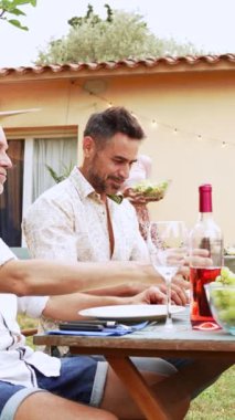 Mutlu, gülümseyen olgun bir kadının dikey portresi. Ev bahçesindeki öğle yemeği partisinde arkadaşlarıyla sağlıklı yiyecekler tutuyor ve paylaşıyor. Yüksek kaliteli görüntüler