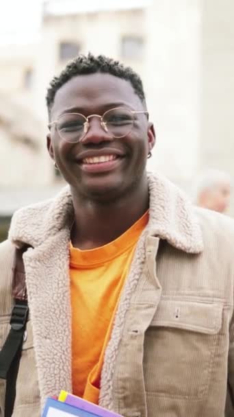 一个年轻的非洲裔美国学生的垂直肖像 带着Googles笑着看着站在高中的相机 在后方地面上一群青少年在走路和笑着 — 图库视频影像