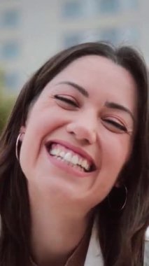 Dikey bireysel olarak, dışarıda duran beyaz dişli, gülümseyen ve kameraya bakan genç bir kadının portresi. Olumlu davranışları olan mutlu genç bir kızın ön yüzü. Yüksek kaliteli görüntüler