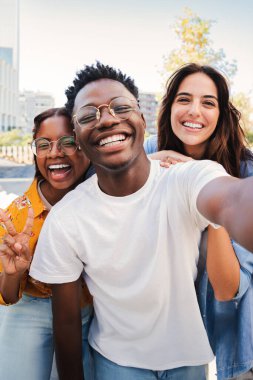 Birlikte selfie çekerken gülümseyen bir grup çok ırklı genç öğrencinin dikey portresi. Mutlu Afro-Amerikan gençliği neşeli arkadaşlarıyla gülüyor. Dostça buluşmada sınıf arkadaşları