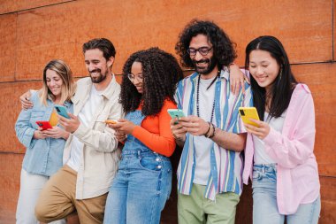 Bir grup arkadaş internette gezinmek için cep telefonu kullanırken eğleniyor. Genç insanlar akıllı telefon sosyal medya uygulaması ile fotoğraf paylaşıyorlar. Arkadaşlar gülümsüyor ve gülüyor cep telefonlarını izliyorlar.