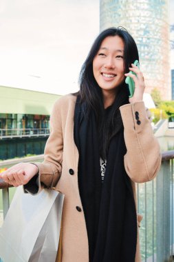 Genç Asyalı bir kadının dikey portresi dışarıda dostça bir telefon konuşması yapıyor. Bir Çinli kız cep telefonuyla gülümsüyor ve konuşuyor. İletişim konsepti. Yüksek kalite
