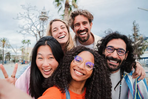 Group of joyful young friends taking a selfie portrait smiling looking at camera together at funny party. Five multiracial happy people on a social gathering bonding outside, enjoying the weekend