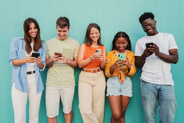 Teal Wall 'da cep telefonu uygulamalarını kullanarak eğlenen ve gülümseyen çok ırklı bir grup genç arkadaş. Gençler sosyal medyada mavi arka planda cep telefonuyla mesajlarını paylaşırken eğleniyorlar. Yüksek