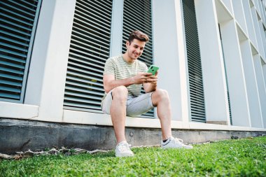 Sosyal medyayı izlemek için cep telefonu kullanan beyaz tenli bir afet. Arkadaşça gülümseyen ve cep telefonu dışarıda otururken video oyunu oynayan genç adam.