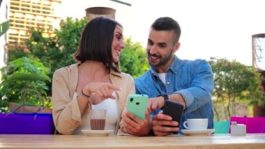 İnternetten alışveriş yapan genç bir çift cep telefonuyla satış yaptığı için çok mutlu. Mele ve kadın bir cep telefonuyla medyayı paylaşırken eğleniyorlar. Kahve dükkanının terasında akıllı telefon izleyen arkadaşlar.