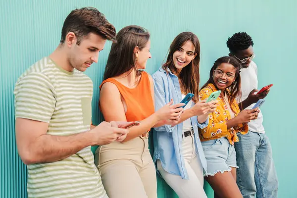 Çok ırklı bir grup mutlu genç arkadaş cep telefonu uygulamalarını kullanarak eğleniyor ve gülümsüyor. Çeşitli genç öğrenciler sosyal medyada içeriği izlerken eğleniyorlar