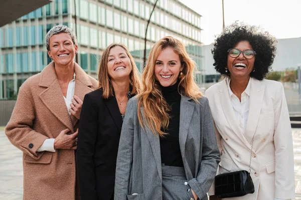 İş yerinde gülümseyen ve kameraya bakan bir grup gururlu iş kadını. Gerçek yönetici kadınlar, takım elbiseleriyle ve başarılı ifadeleriyle birlikte gülüyorlar. Şirket kadın çalışanları toplantısı