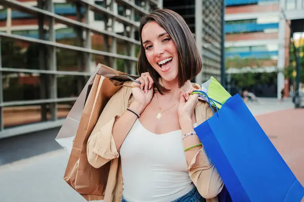 Close up portrait of a young woman holding shopping bags and looking excited at camera. Joyful customer female enjoying a discount purchase. Lady smiling buying a retail. Buyer girl at sale store