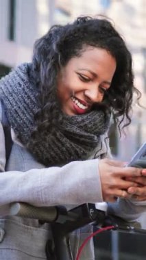 Ofis dışında akıllı telefondan mesaj atan genç bir kadının dikey portresi. Gülümseyen kız cep telefonu uygulaması kullanarak eğleniyor. Yüksek kaliteli görüntüler