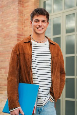 Lisede kameraya bakan popüler bir çocuğun dikey portresi. Önüne bakan gerçek bir genç erkek öğrenci. Üniversite kampüsündeki yakışıklı adam. Akademideki genç yetişkin çocuk.