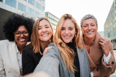 Bir grup başarılı iş kadını gülümseyip selfie çektirirken eğleniyor. Kameraya bakan girişimci bayanların takım çalışması. Mutlu başlangıç yöneticileri işe gülen kadınlar
