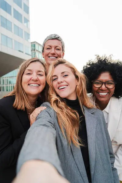 Dikey portre. Bir grup başarılı iş kadını gülümsüyor ve selfie çekerken eğleniyor. Kameraya bakan girişimci bayanların takım çalışması. Yeni başlayanlar için mutlu bayanlar işte gülüyorlar.