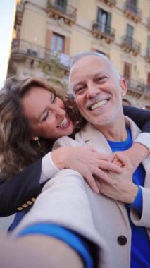 Yetişkin evli bir çiftin kameraya bakıp gülümsediği dikey bir video çağrısı. Orta yaşlı partnerler mutlu bir ifadeyle öne bakıyor. Orta yaşlı karı ve koca. Eş ve gri saçlı adam. Yüksek