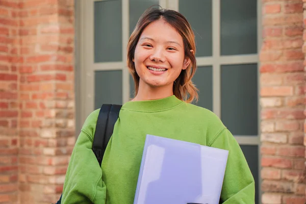 Individual portrait of a young asian high school student girl smiling and looking at camera. Chinese teenage female staring front at university campus. Thai classmate woman with happy expression. High