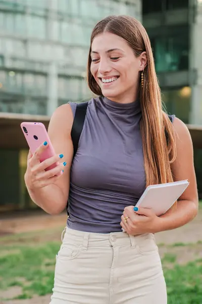 一个快乐的少女笑着用智能手机在户外用社交媒体应用程序打字的垂直肖像 年轻女人在用手机发短信很开心 真正的女士用手机 — 图库照片