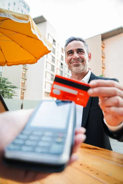 Vertical Happy mature business man paying bill using a contactless credit card in a restaurant. Handsome mid adult male smiling holding a creditcard and giving a payment transaction to the cashier
