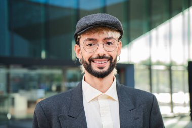 Hipster bir adamın kişisel portresini yakın çekim yapın. Gülümseyen ve dışarıda kameraya bakan. Arkadaş canlısı ve olumlu ifadeli genç bir adamın ön görüntüsü. Mutlu orijinal havalı erkek dik dik bakıyor.