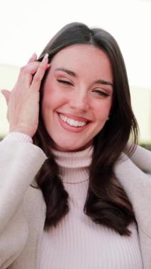 Dikey. Beyaz dişli, gülümseyen ve kameraya bakan beyaz bir kadın. Açık havada duran beyaz elbiseli güzel, mutlu bir kadının portresi. Yüksek kalite 4 bin yavaş çekim