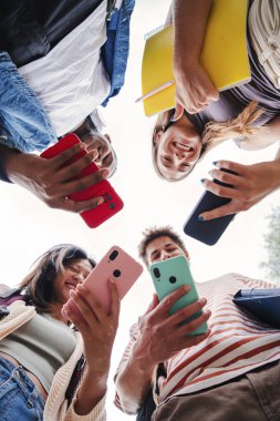 Cep telefonu uygulamalarını kullanarak eğlenen ve gülümseyen çok ırklı genç arkadaşların dikey düşük açılı görüntüsü. Akıllı bir telefonu tutan bir öğrencinin portresi. Meslektaşlar cep telefonlarıyla paylaşılıyor