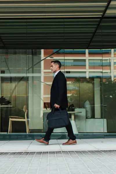 Vertical full length portrait of a mature business man walking and holding a laptop bag. Mid adult financial executive male going to the office. Handsome corporate business person with a briefcase