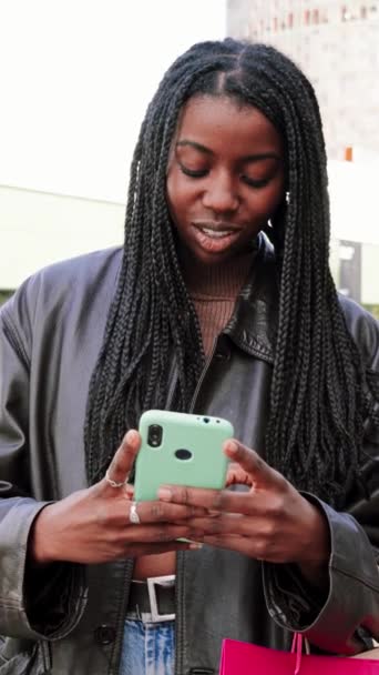 垂直に 若いアフリカ系アメリカ人女性が笑顔で 携帯アプリでタイピング 幸せな10代の少女は 屋外で買い物した後 スマートフォンを使用してメッセージを送信します コミュニケーションのコンセプト スローモーション — ストック動画