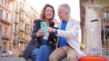 Orta yaşlı bir çift oteli cep telefonuyla arıyor. Dışarıda oturan bir uygulama kullanıyor. Olgun insanlar sosyal medya uygulamasında cep telefonuyla eğleniyorlar. Akıllı telefonlu orta yaşlı arkadaşlar.