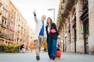 Tatillerde bavulla birlikte yürüyen olgun turistler. Orta yaşlı çift şehir merkezindeki bir Avrupalıyı gezerken eğleniyor. Gerçek orta yaşlı evli insanlar tatillerde seyahatin tadını çıkarıyorlar. Yüksek