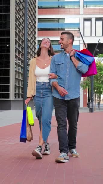 垂直的 一对快乐的年轻夫妇享受着销售日 在中央购物中心观看零售 促销和打折 男朋友和女朋友一起散步 笑着提购物袋 — 图库视频影像