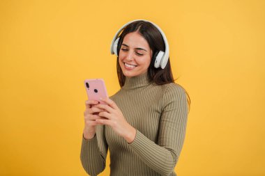 Gülümseyen mutlu genç kadın akıllı telefonunu kullanıyor ve internette sohbet ediyor ya da sarı arka planda internette geziniyor. Genç beyaz kadın cep telefonu uygulamalı komik videolar izliyor. Yüksek