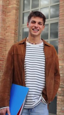 Üniversite kampüsünde gülümseyen ve kameraya bakan bir gencin dikey portresi. Lisedeyken yüzünde olumlu bir ifadeyle ayakta duran ve dik dik bakan adam. Kendinden emin, mutlu genç adam.