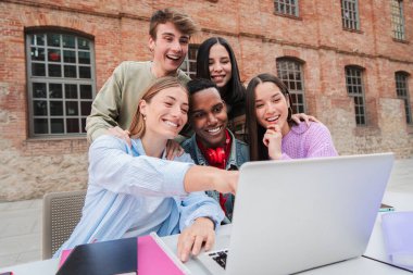 Lise ev işleri hakkında bilgi toplamak için dizüstü bilgisayarla gülümseyen bir grup çok ırklı genç öğrenci. Sınava çalışan sınıf arkadaşları kampüsteki bir dizüstü bilgisayarda ders izliyorlar.