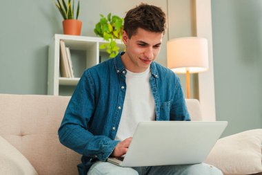 Gündüz vakti evde dizüstü bilgisayarla çalışan mutlu bir serbest çalışan. Oturma odasında bilgisayarla gülümseyen ve internette gezinen genç bir adam. Girişimci banka finansmanı ve yatırımları arıyor