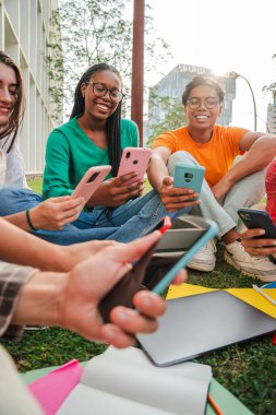 Dikey. Üniversite kampüsünün bahçesinde oturan bir grup öğrenci cep telefonlarını birlikte kullanarak eğleniyorlar. Gençler sosyal medyada akıllı telefonlarıyla video paylaşıyorlar. Telefonu olan arkadaşlar