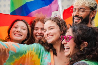 Eşcinsel onur gününü gökkuşağı bayrağıyla kutlayan bir grup LGBT çükünün yakın portresi. Genç yetişkin LGTB arkadaşları cinsel haklar partisinde özgürlük ve cesaret ifadesiyle gülümsüyor