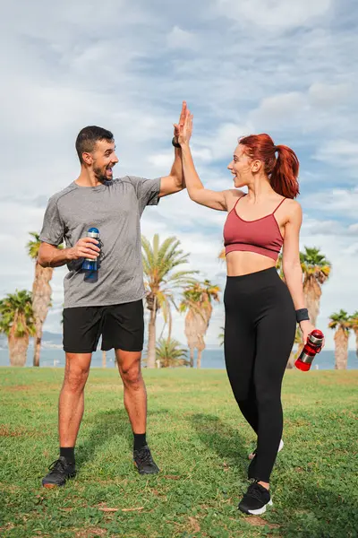 Dikey. Sportif çiftler, kardiyo çalışmaları sırasında bir dönüm noktası elde ettikten sonra gülümseyip beşlik çakıyorlar. Güçlü erkek ve atletik kadın kas eğitimine beş veriyor. Arkadaşlar refahın tadını çıkarıyor.