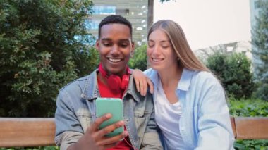 Genç, çok ırklı bir çift cep telefonuyla internette gezinirken eğleniyor. Sosyal medya uygulamasını paylaşmak için akıllı telefon kullanan iki genç arkadaş. Gençler cep telefonu ekranını izliyor. Yüksek