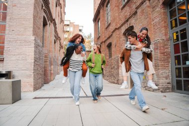 Bir grup erkek öğrenci, kız arkadaşlarına sırtına biniyor, yürüyor ya da sınıfa koşuyor. Heyecanlı çok ırklı sınıf arkadaşları üniversite kampüsünde birlikte eğleniyorlar. Okula dönelim. Yüksek